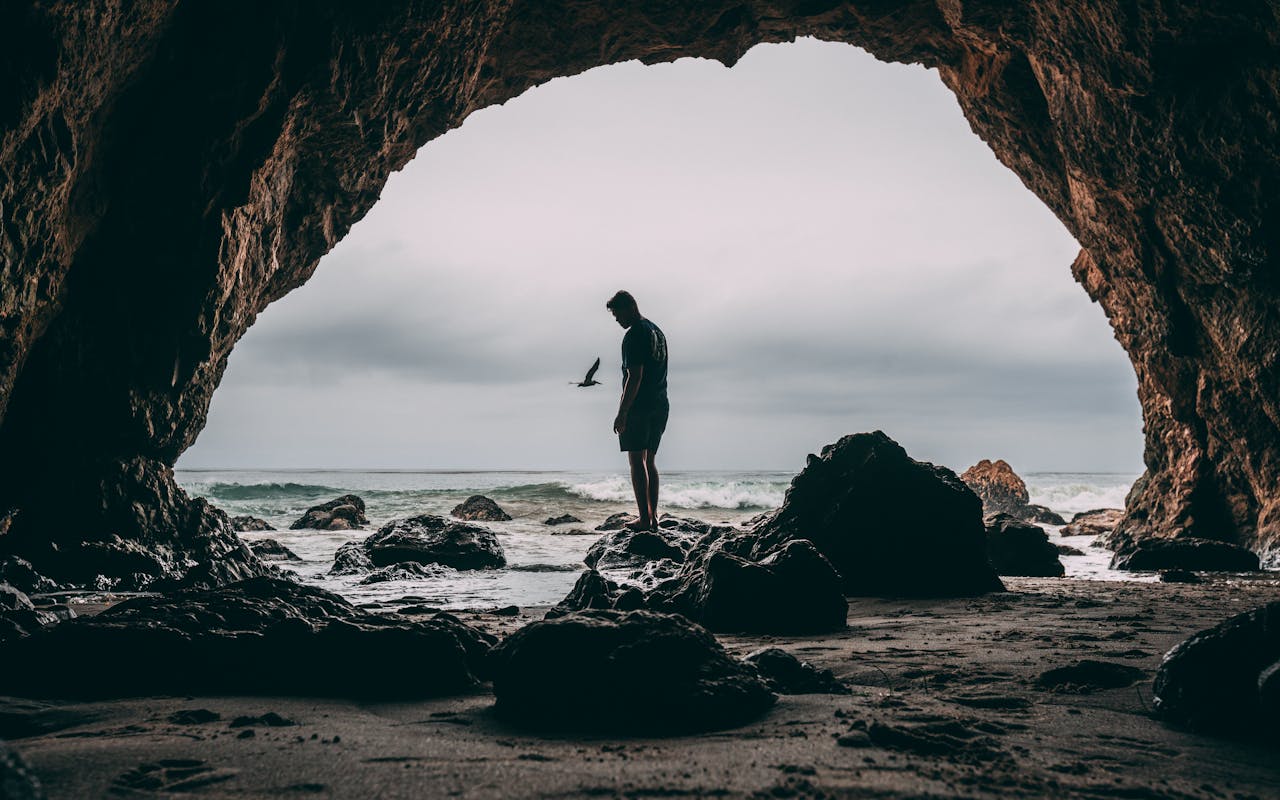 The Art of Drawing Readers In: Your attractive post title goes here Silhouette of a person standing in a sea cave at Malibu beach, with ocean waves and rocks creating a dramatic scene.