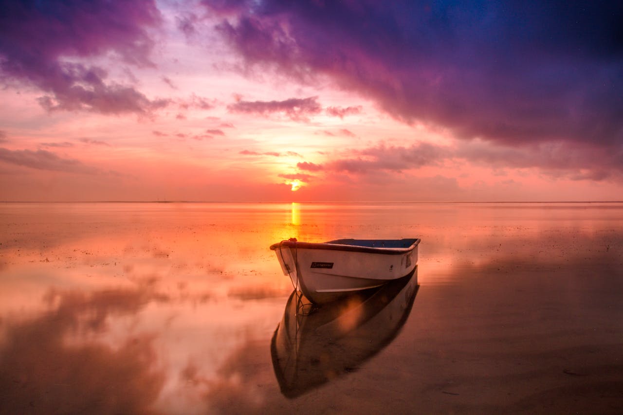 contact-img A tranquil scene of a boat at sunset with vivid sky reflecting on calm waters.
