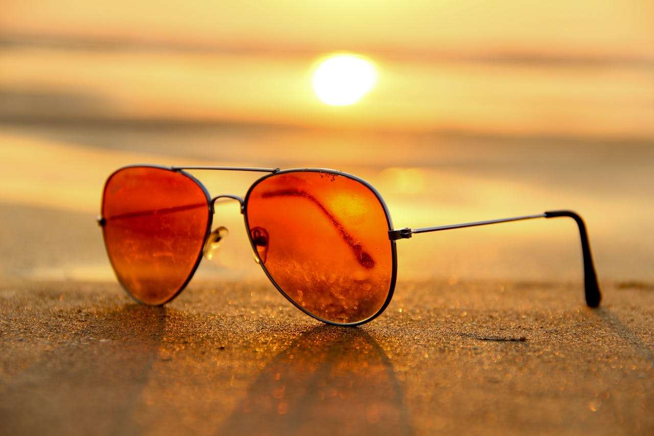 gallery-5 Close-up of sunglasses on a beach during a vibrant sunset, capturing the essence of summer.